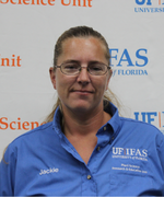 A woman wearing glasses and a blue collared shirt smiles at the camera.