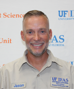 A man with short brown hair smiles at the camera wearing a tan collared shirt.