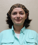 A woman with short brown hair smiles at the camera wearing a light blue collared shirt.