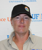 A woman wearing glasses and a blue collared shirt smiles at the camera.
